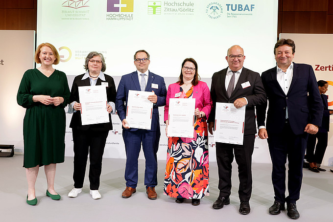 The Federal Minister for Family Affairs and representatives of the certified universities stand on the stage and hold their certificates in their hands.