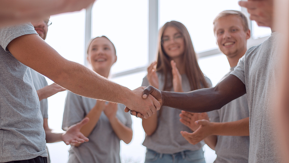 Young people stand in a circle and shake hands.