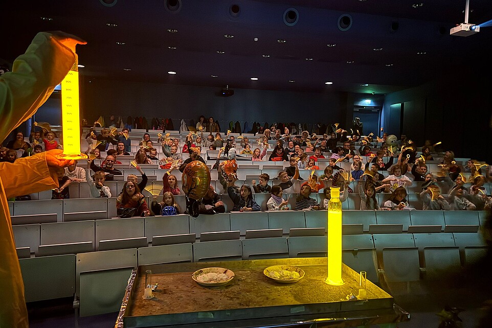 Ein Leuchtexperiment mit gelber Neonfarbe findet auf der Bühne statt.