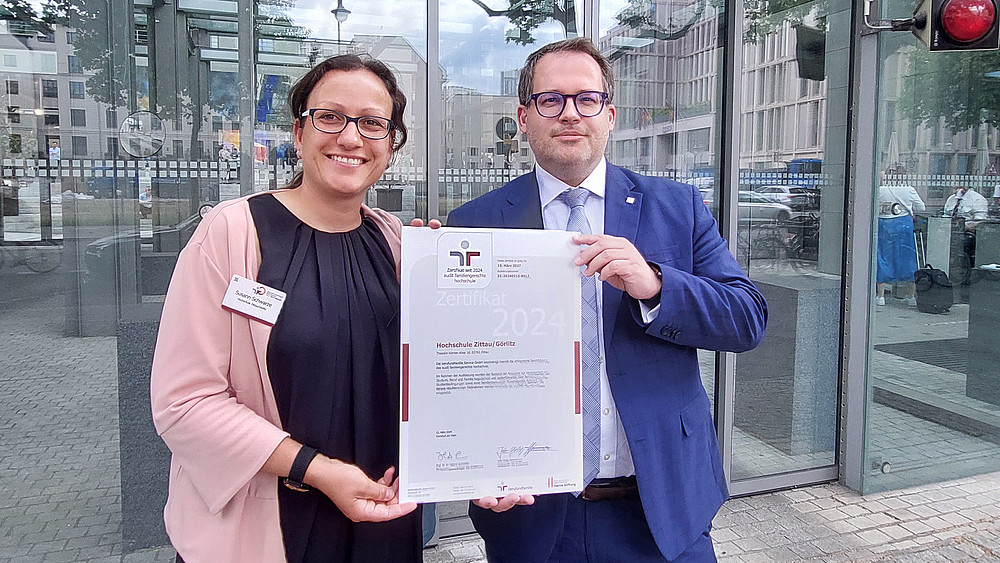 Susann Schwarze und der Rektor halten das Zertifikat zur familiengerechten Hochschule in die Höhe.