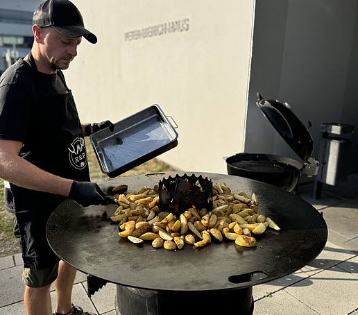 A man grills potato wedges on a barbecue barrel.