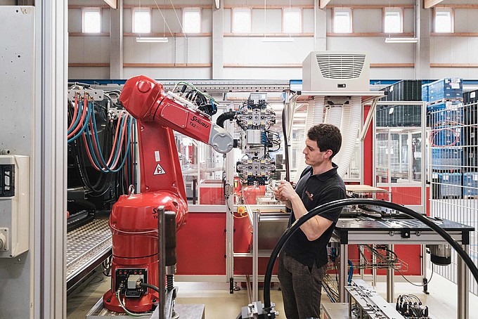 Mann in einem schwarzen Poloshirt arbeitet an einem industriellen Roboterarm.