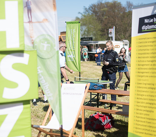 HSZG-Würfel und Banner auf der Festwiese des Europafests. Im Hintergrund spielen zwei Polizisten Tischtennis.