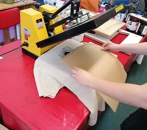 A screen printing machine into which a white T-shirt is clamped, on which baking paper has just been placed.