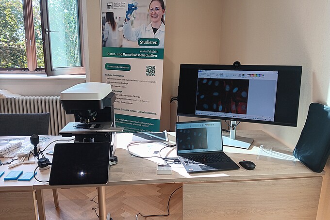 Mikroskop, Laptop und Monitor zeigen vergrößerte Zellaufnahmen am biomedizinischen Forschungsstand der HSZG.