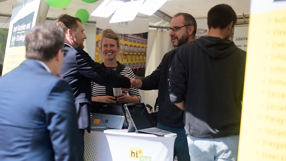 Der Ministerpräsident und Prorektor schütteln sich Hände am HSZG-Stand.