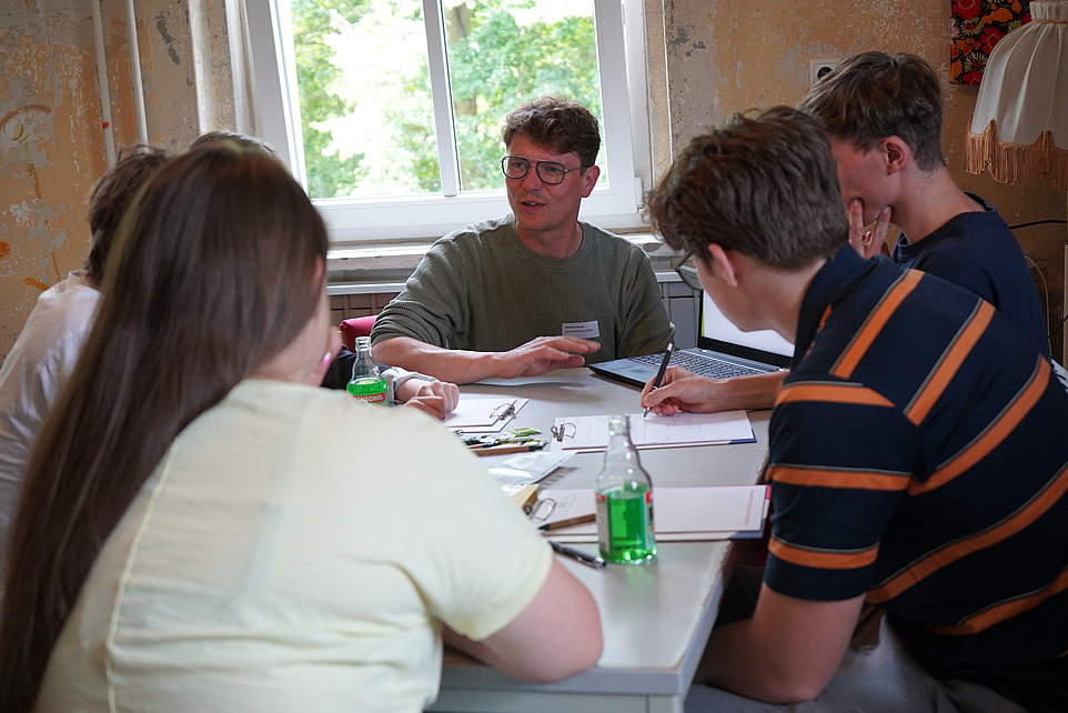 Sebastian Benad sitzt an einem Tisch und diskutiert mit einer Gruppe junger Menschen in einem Workshop.