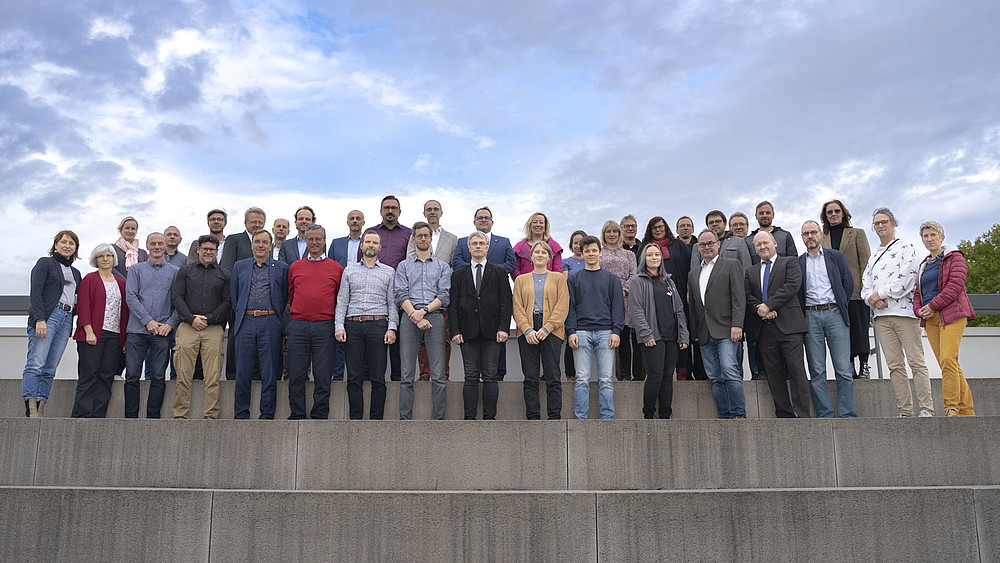 Auf einer Dachterrasse stehen die Mitglieder des Erweiterten Senats in mehreren Reihen auf Steintreppen.