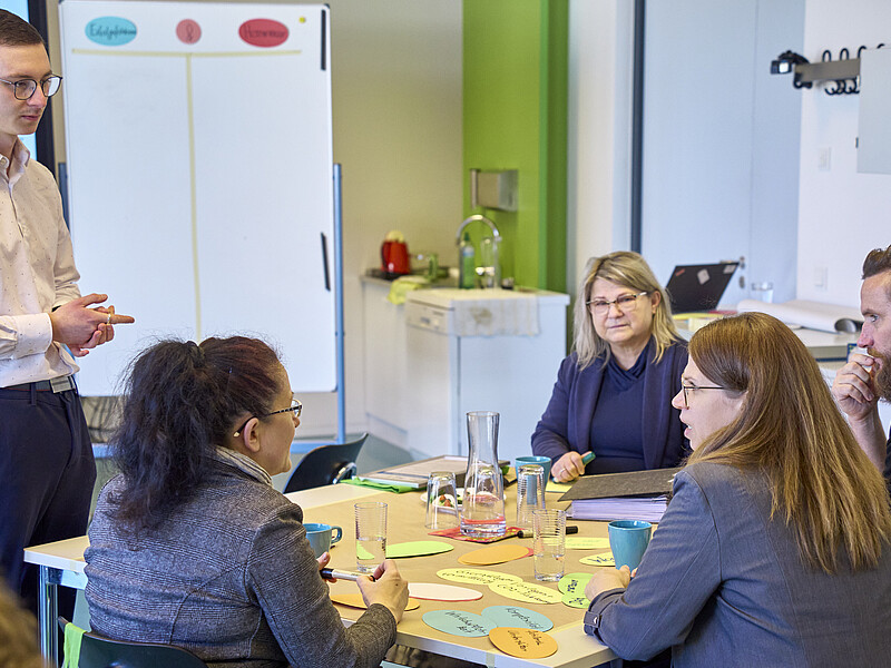An einem Projekttisch sitzen Vertretende von Unternehmen. Ein HSZG-Ansprechpartner steht neben einem weißen Flipchart.